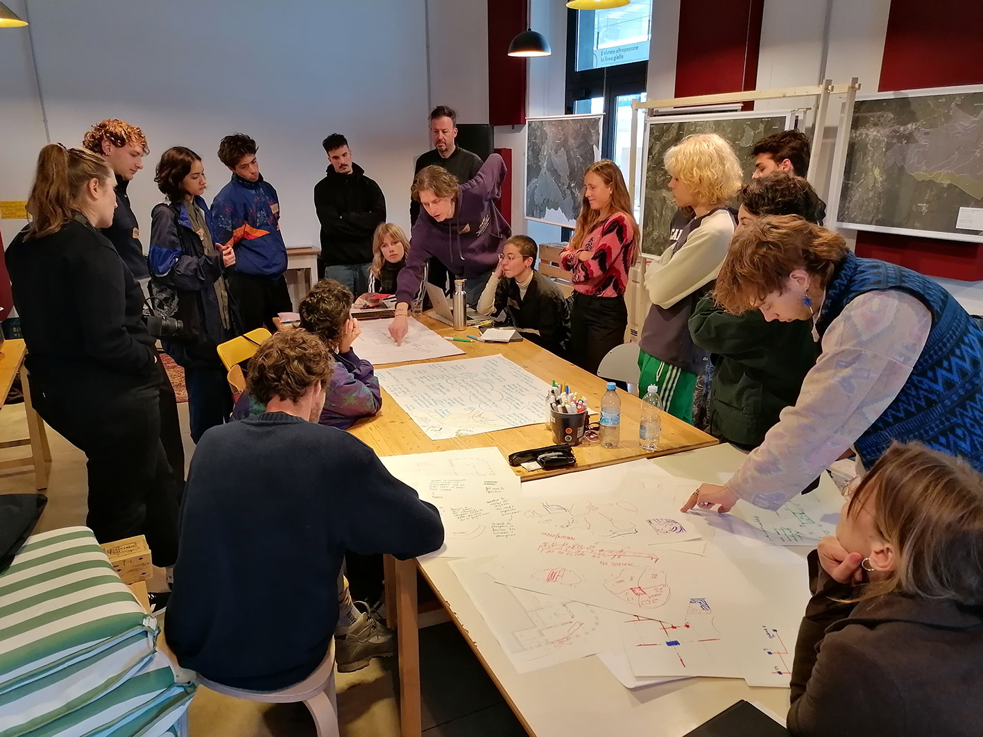 A group of architecture students standing around a table with maps of the Station for Transformation spaces.