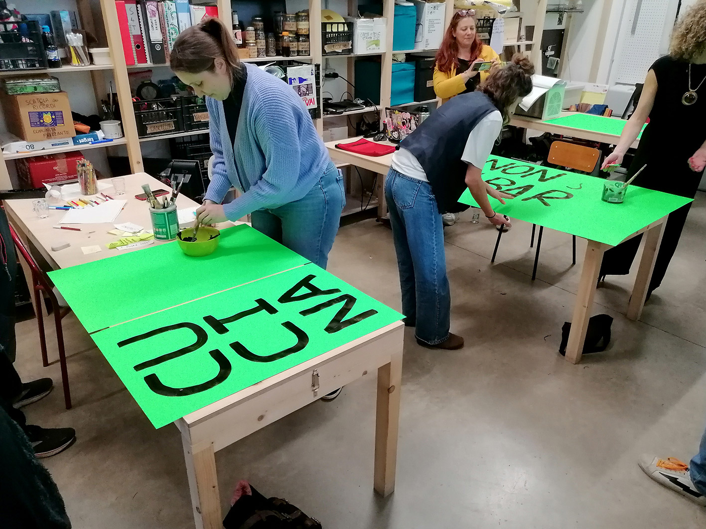 Three people painting keywords on large neon green sheets.