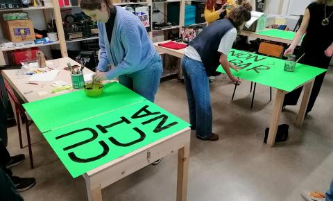 Three people painting keywords on large neon green sheets.