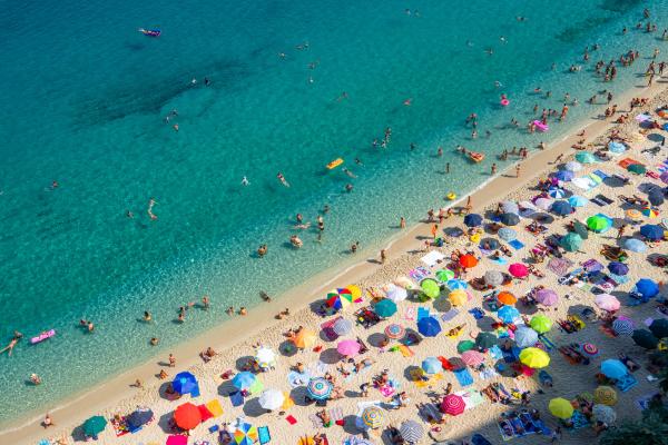 Pogled od zgoraj na živahno plažo z množico pisanih senčnikov in kopalcev v turkiznem morju.